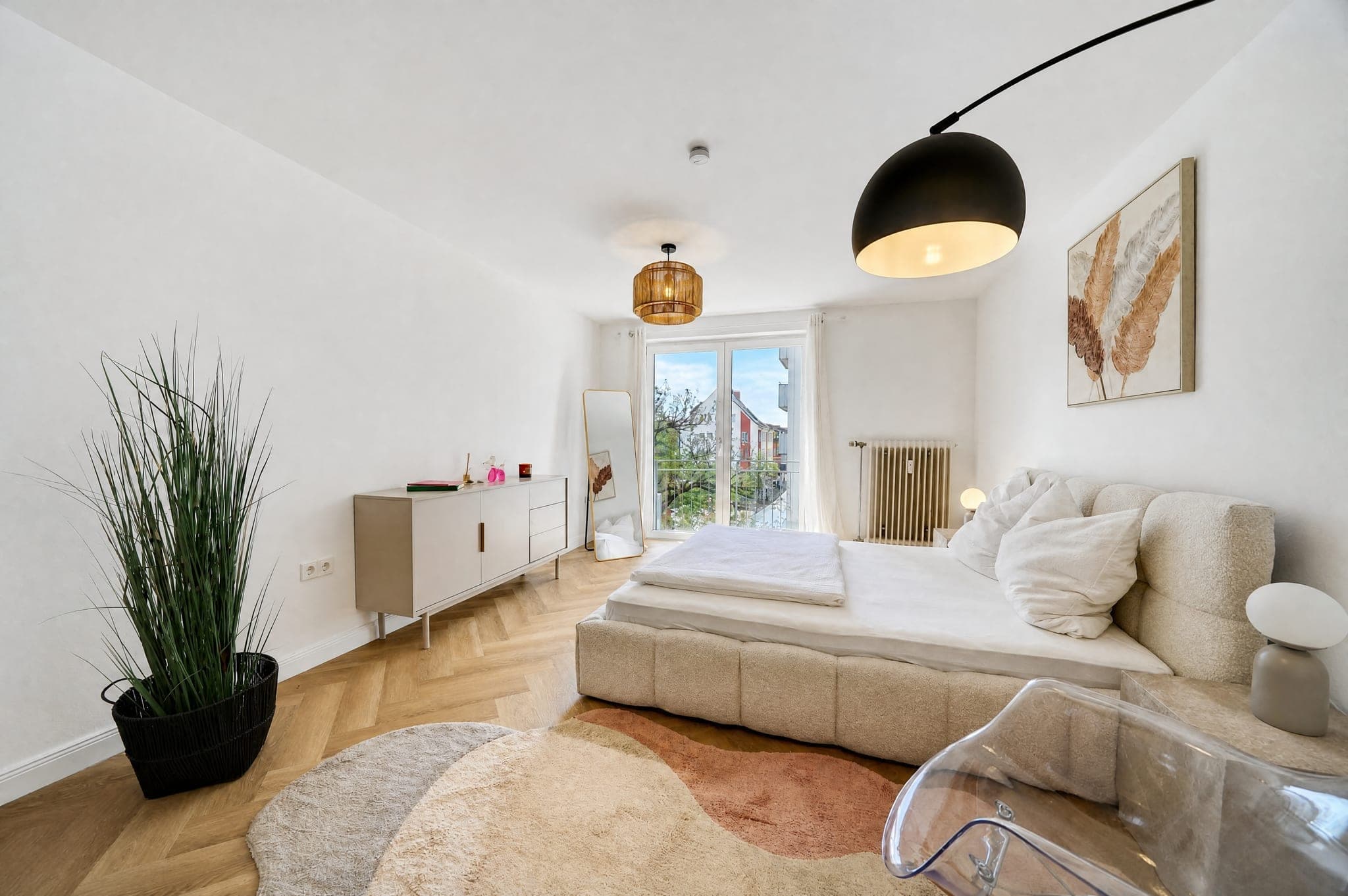 Schlafzimmer mit gepolstertem Bett, Sideboard und Standspiegel auf Fischgrätparkett