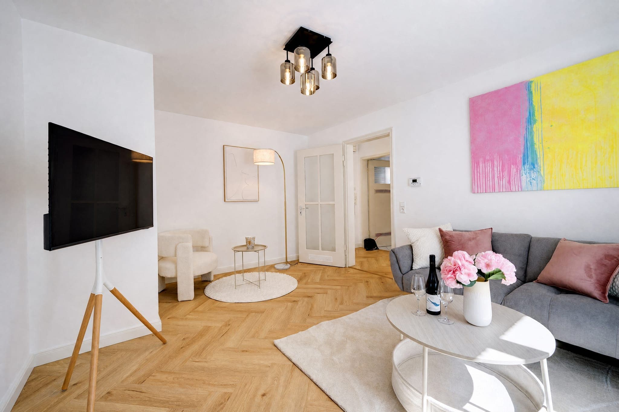 Wohnbereich mit Wandfernseher, grauem Sofa und runden Beistelltischen