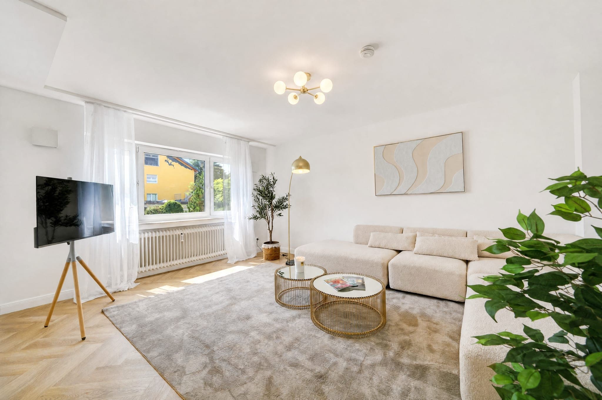 Wohnzimmer mit modularem Sofa, Fernseher und Fensterfront ins Grüne