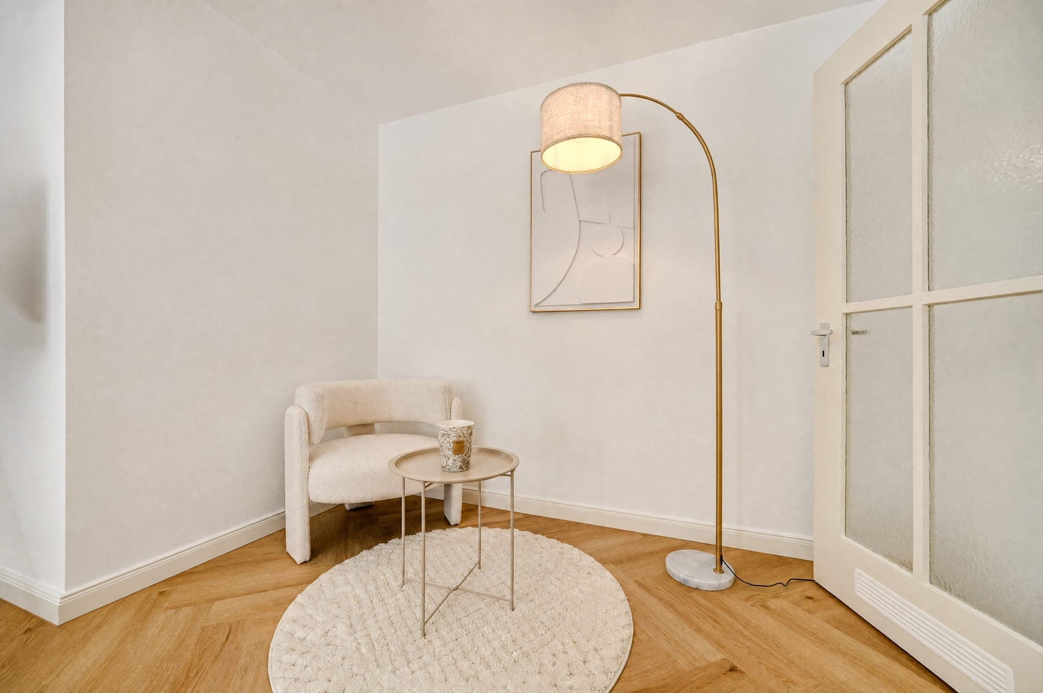 Sitzecke mit Polstersessel, Beistelltisch und Bogenlampe vor heller Wand