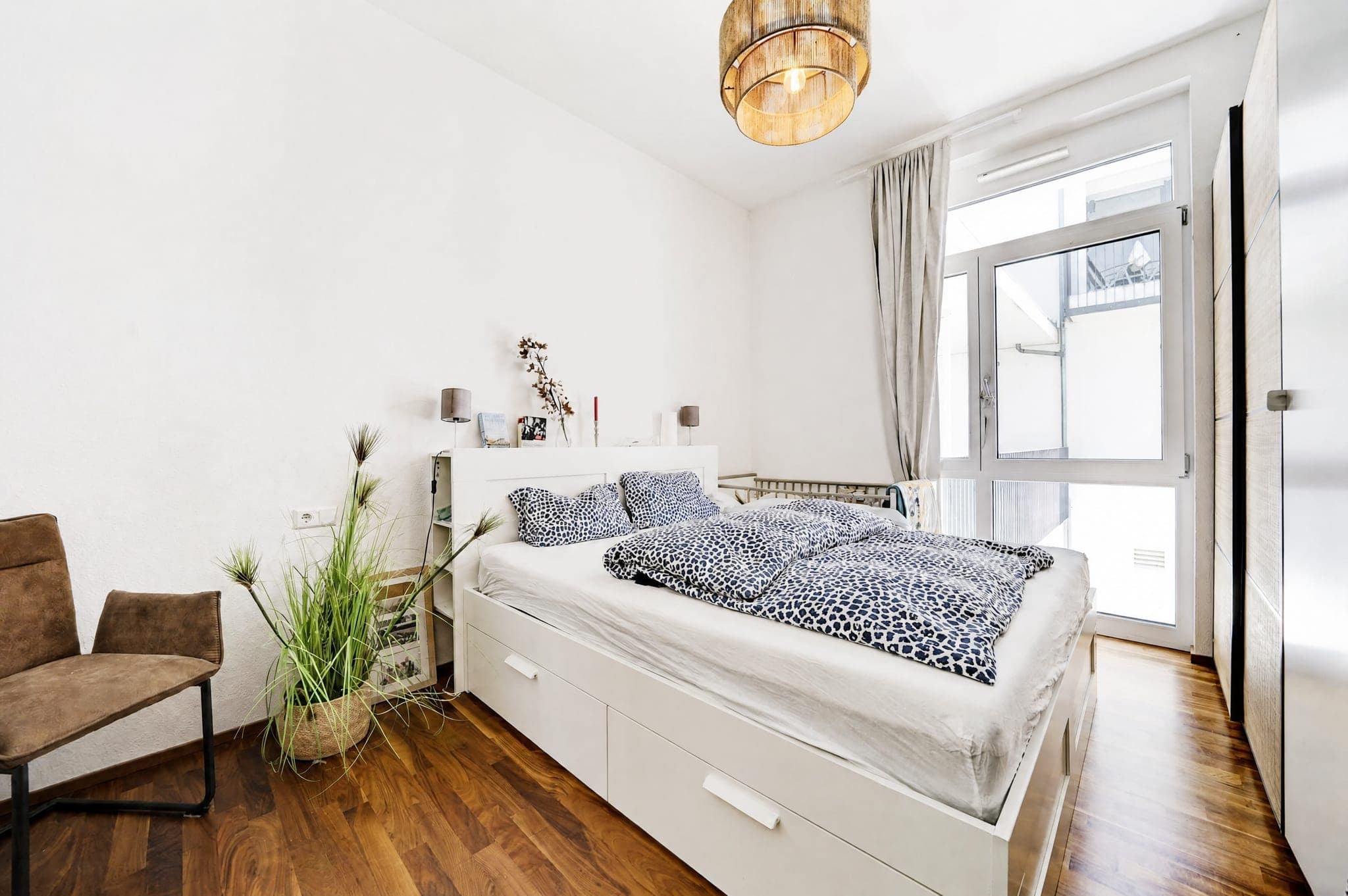 Schlafzimmer mit Bettkasten, gemusterter Bettwäsche und Balkontür