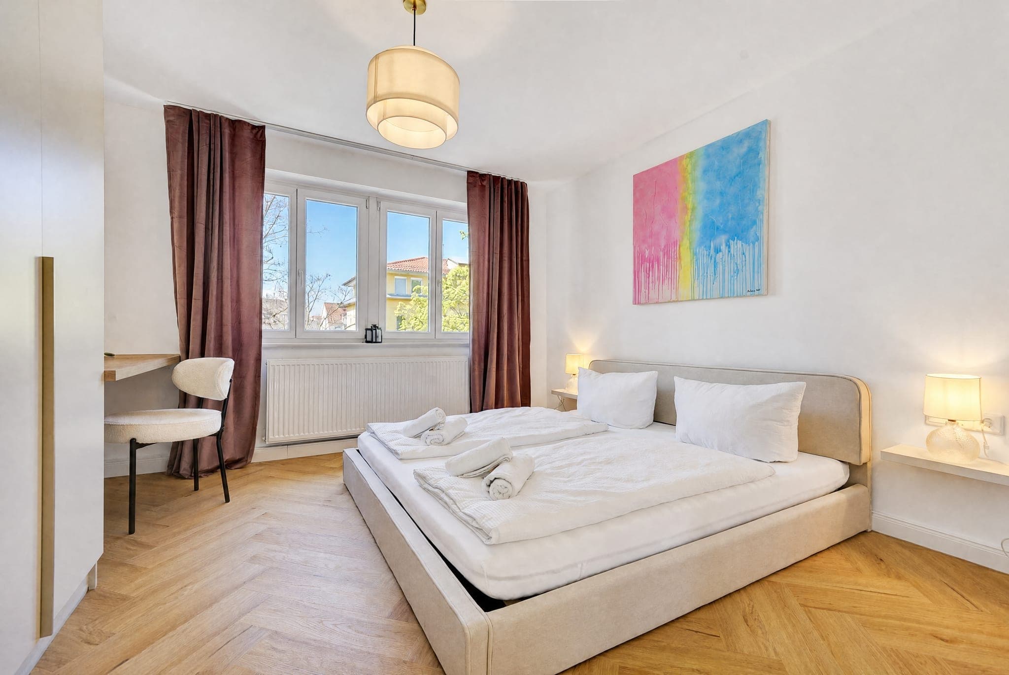 Schlafzimmer mit Doppelbett, bordeauxroten Vorhängen und Blick über die Nachbardächer