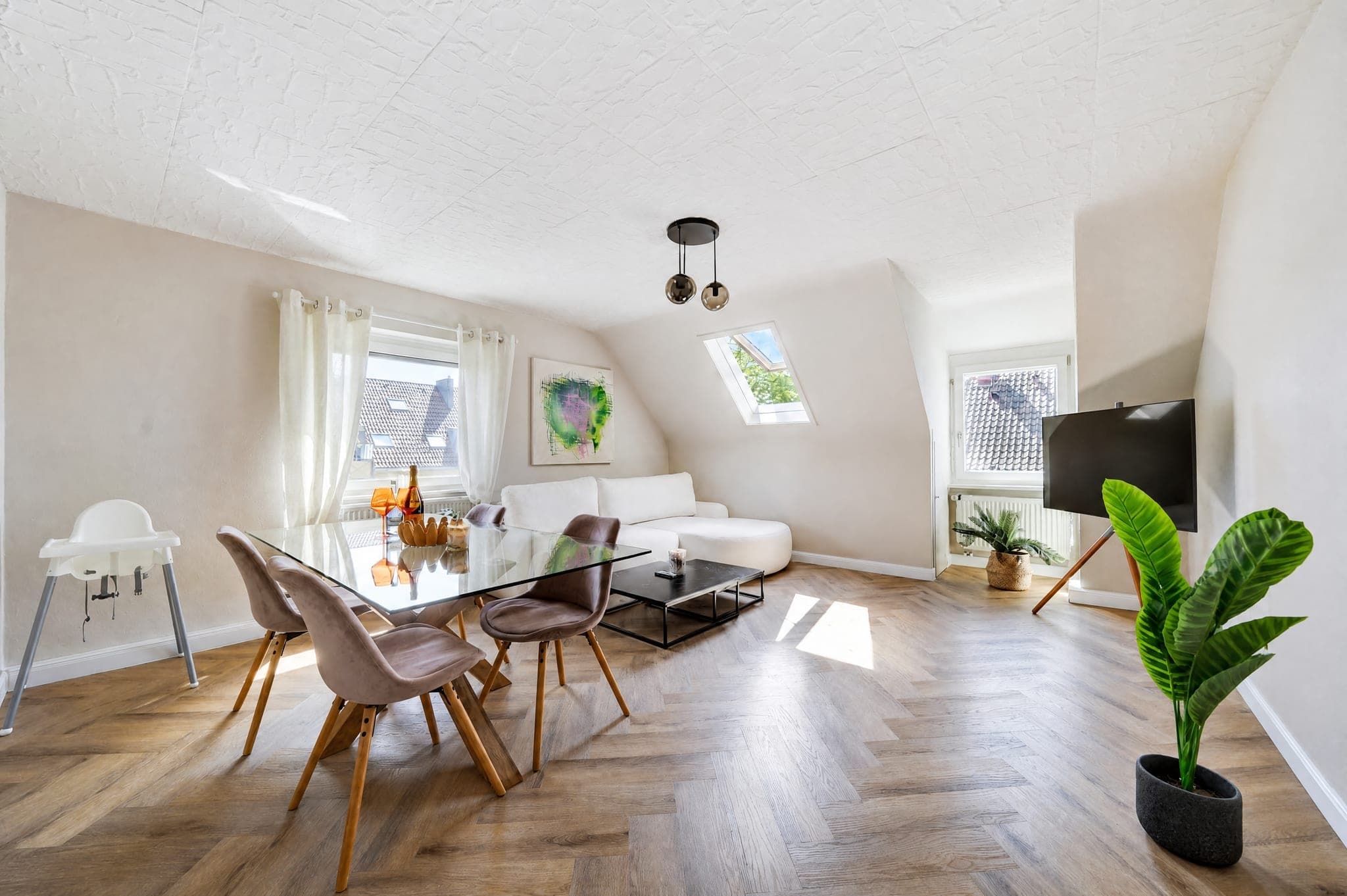 Essbereich mit Glastisch und Hochstuhl neben dem Sofa unter der Dachschräge