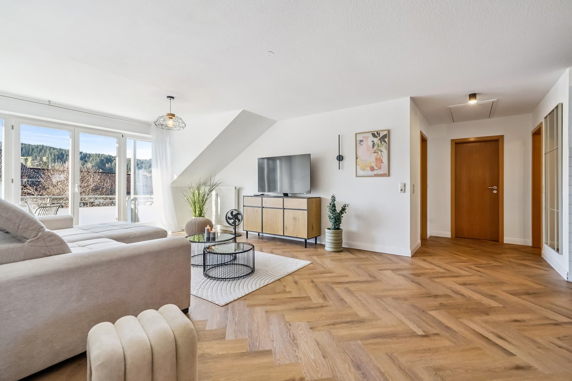 Dachgeschoss-Wohnzimmer mit hellem Sofa, TV-Sideboard und Fensterfront ins Grüne