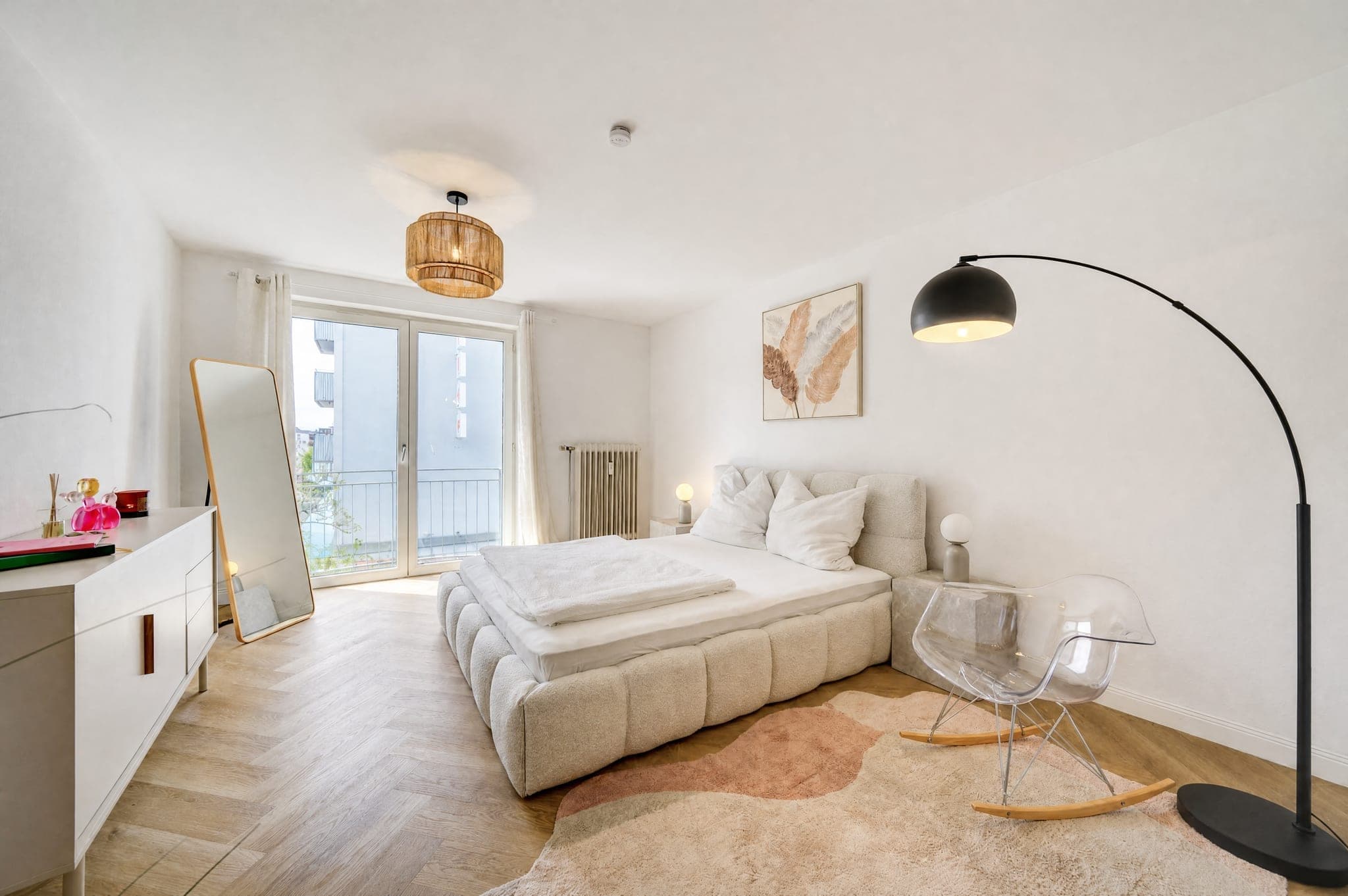 Schlafzimmer mit Polsterbett, Standspiegel und Balkontür; das Gegenlicht am Fenster bleibt gezeichnet