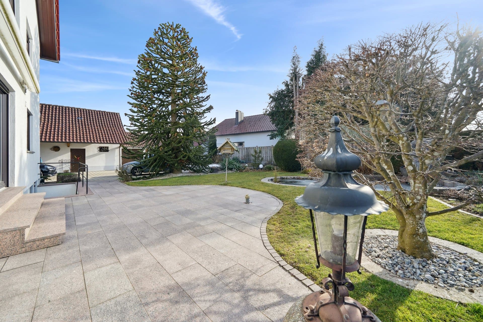 Gepflasterte Hofeinfahrt mit Gartenlaterne vor dem Wohnhaus, Ziegeldach gegen blauen Himmel